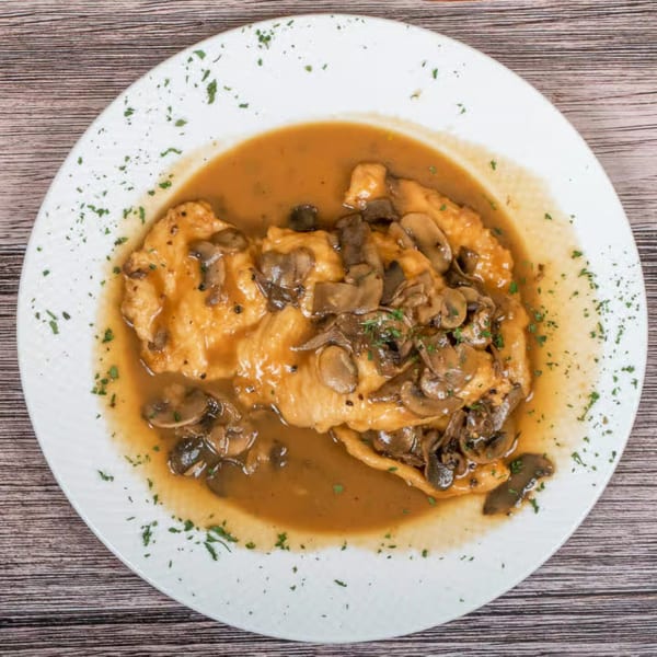 Chicken and mushrooms in a rich brown sauce, garnished with parsley on a white plate.