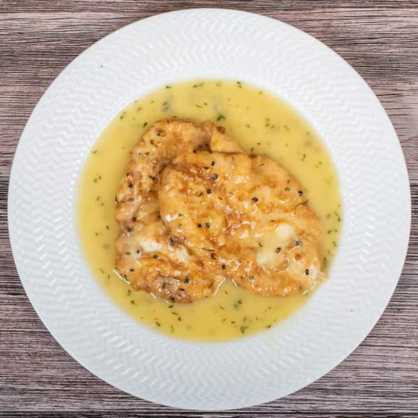 Two pieces of golden-brown chicken or fish in a yellow, herb-flecked sauce on a white plate.